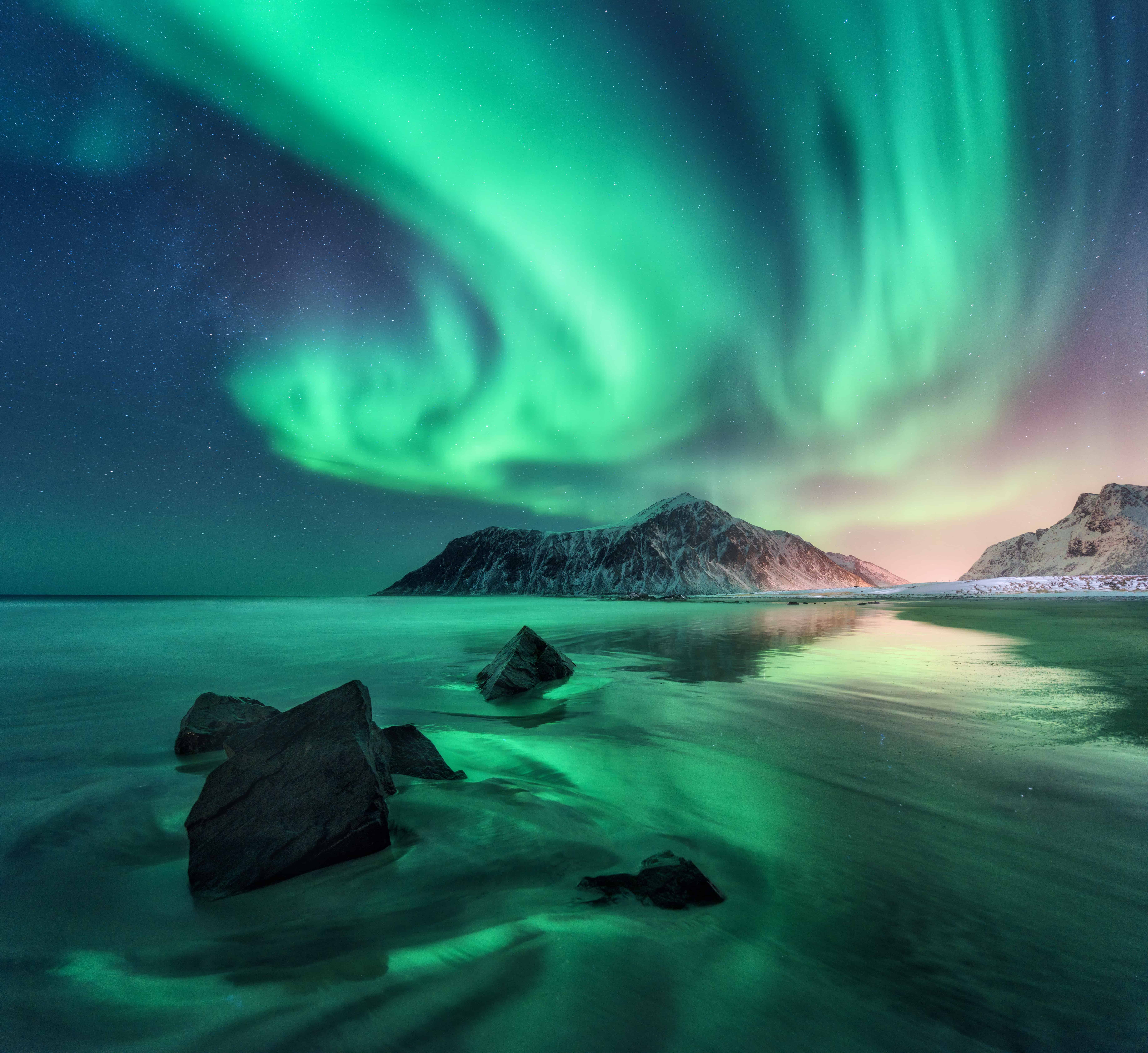 Aurora. Northern lights in Lofoten islands, Norway. Sky with polar lights, stars. Night winter landscape with aurora, sea with sky reflection, stones, sandy beach and mountains. Green aurora borealis • Travel with Bradley